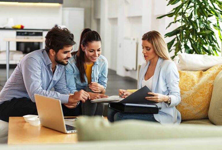 A family reviews insurance documents at their dining table with a laptop and coffee mugs.
